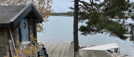 A wooden cabin with a dock extending into a lake, surrounded by trees and autumn foliage.
