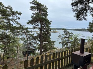 A wooden deck with a metal stove, overlooking a lake with trees and a distant shoreline. - 3 Person Holiday Home in Orno (Orno)