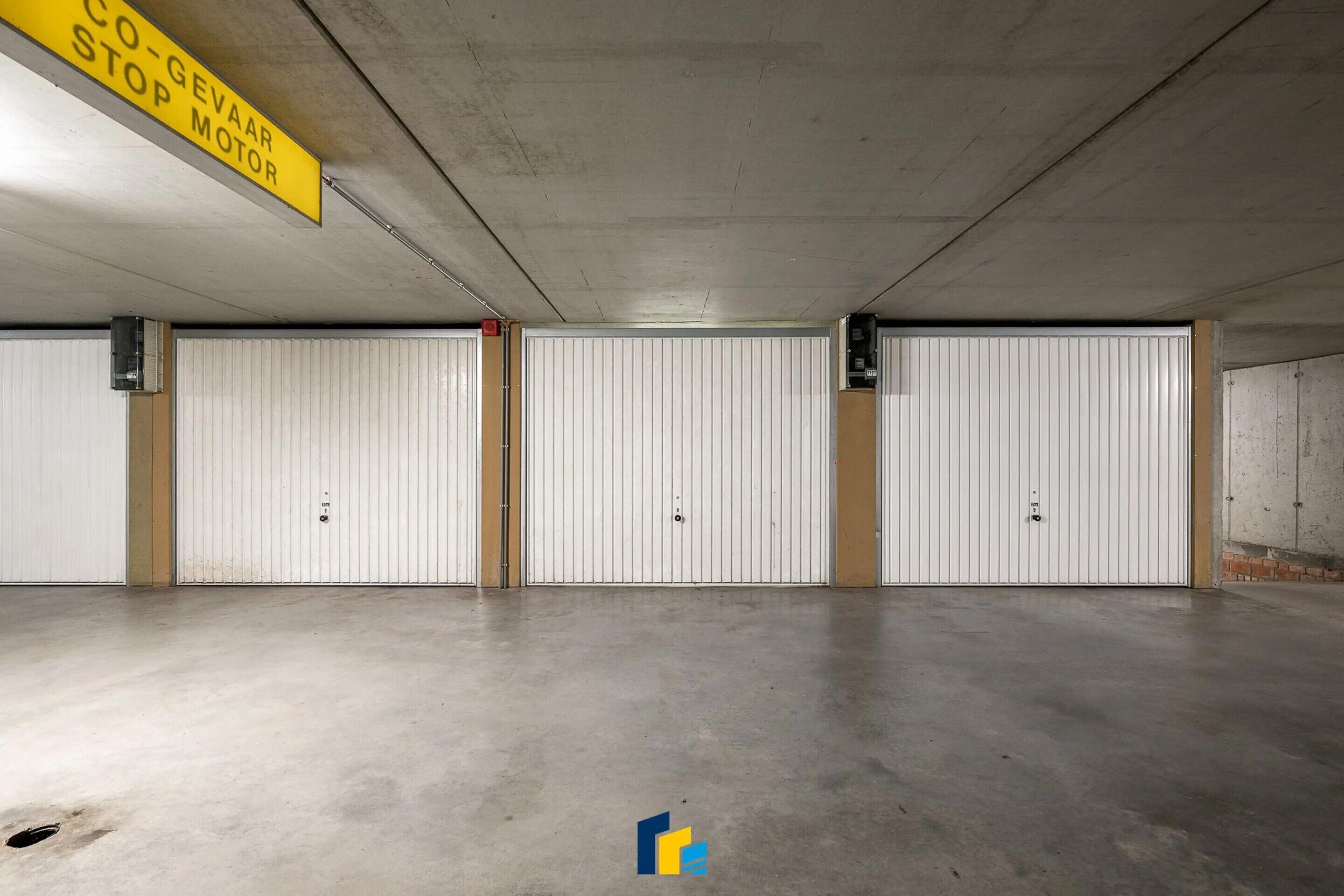 A parking garage with three white doors, a yellow sign indicating a co-geaar stop motor, and a concrete floor.