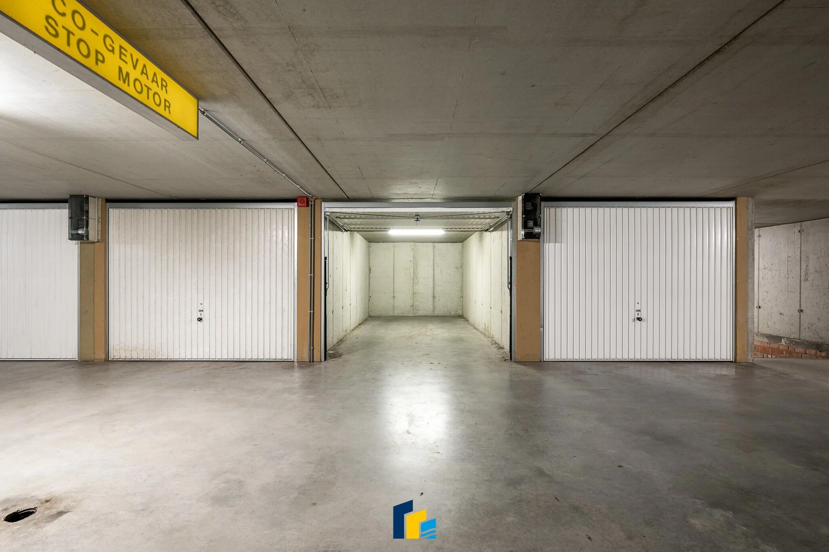 Un garaje para estacionar con puertas blancas, un letrero amarillo que indica zona de parada para motores, y un piso de concreto.