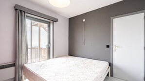 Een slaapkamer met een bed, een raam met gordijnen, een deur en een lamp.