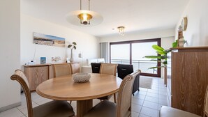 A dining area with a round wooden table, chairs, and a hanging light fixture. - Apartment in Blankenberge With Sea Views (Blankenberge)