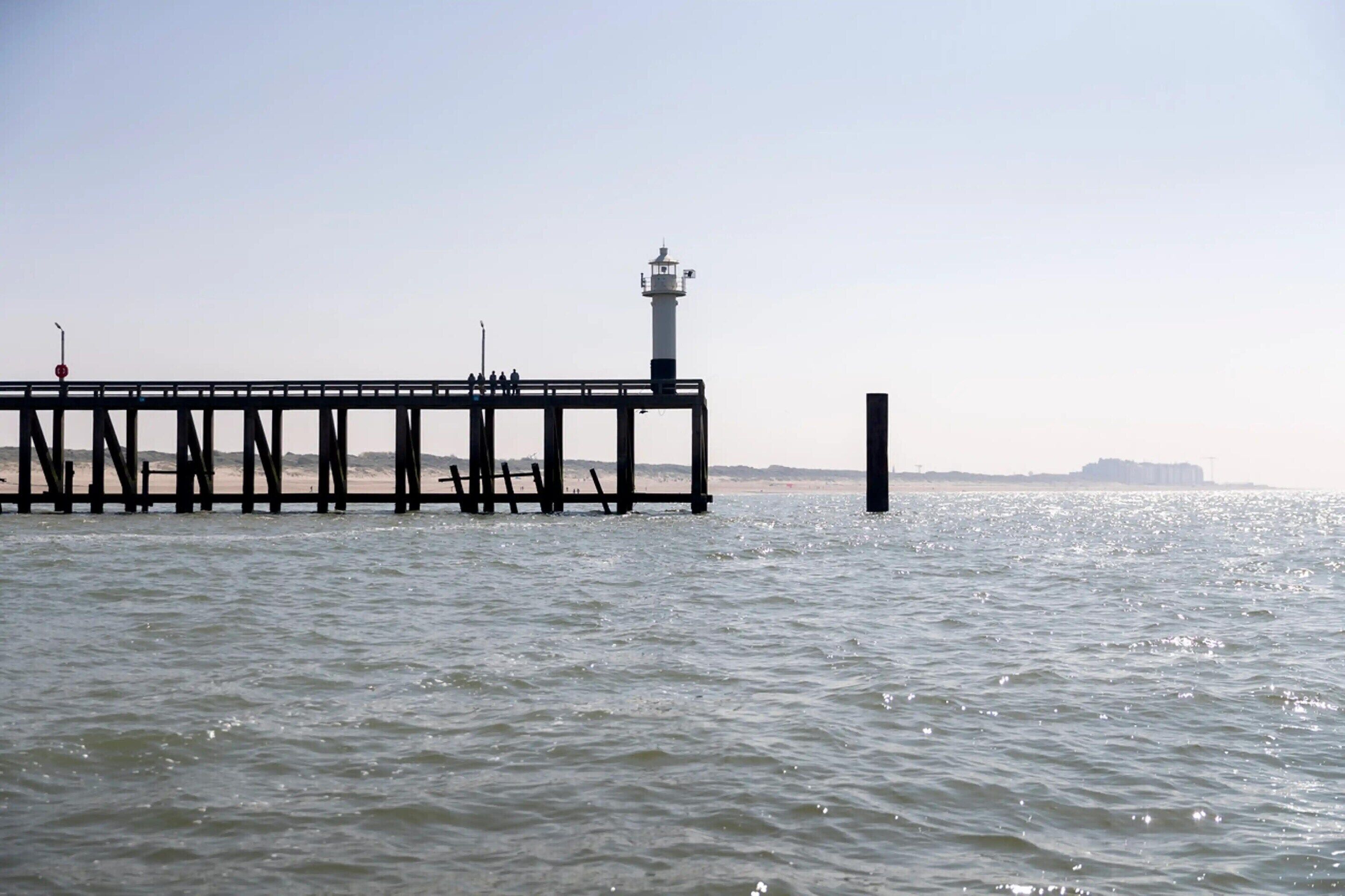A pier extending into calm waters with a lighthouse at the end.