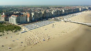 An aerial view of a coastal city with a long beach, numerous beach umbrellas, and a pier extending into the water. - Apartment in Blankenberge With Sea Views (Blankenberge)