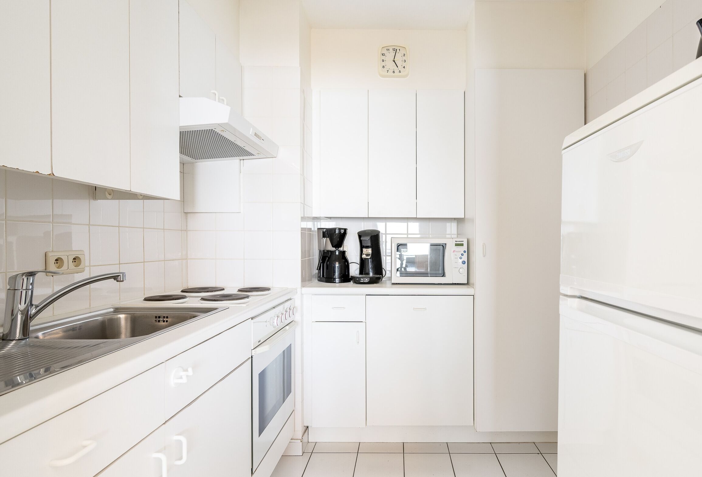 A modern kitchen with white cabinets, a stainless steel sink, a microwave, and a coffee maker.