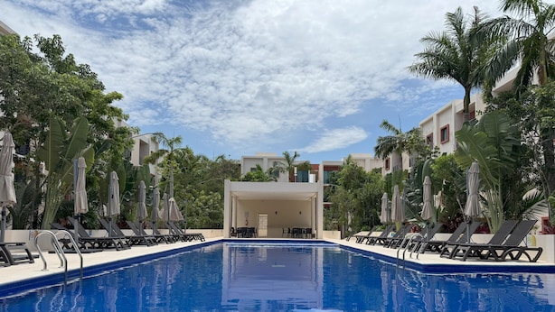 A swimming pool with lounge chairs and umbrellas, surrounded by palm trees and buildings. - Modern apart in Cancun, well located, amenities. 2 bedrooms and 2 full bathrooms (Cancún)