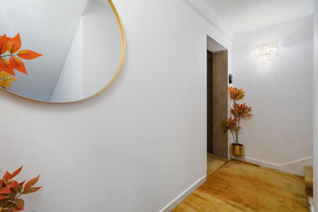 A hallway with a round mirror, a potted plant, and a chandelier.