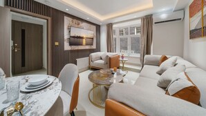 A modern living room with a sofa set, a dining table with plates and cutlery, a coffee table, and a large window with curtains. - Chic & Modern Apartment in Prime Mayfair H2 (London)