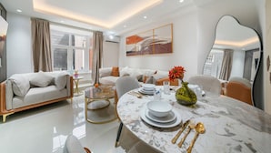 A modern living room with a sofa, a dining table set with plates, glasses, and cutlery, and a large mirror on the wall. - Chic & Modern Apartment in Prime Mayfair H2 (London)