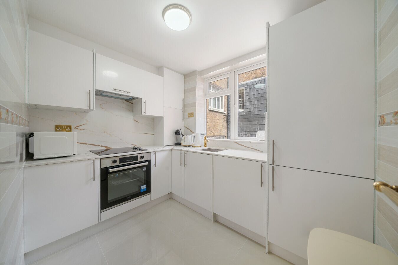 A modern kitchen with white cabinets, a built-in oven, a microwave, and a window with a view of the outside.