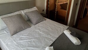 A neatly made bed with white linens and two pillows, a grey upholstered bench with a towel, and a wooden door with a mirror. - Villa with private pool (Orihuela Costa)