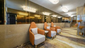 A hotel lobby with a long reception desk, multiple seating areas with cushioned chairs, and a patterned carpet.