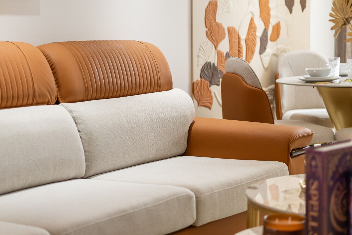 Een moderne zithoek met een bank en fauteuils, een eettafel met een vaas, en een decoratief wandobject.