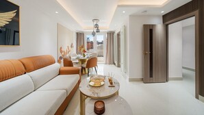 Ein modernes Hotelzimmer mit einer Couch, einem Esstisch mit Stühlen, einem kleinen runden Tisch mit Kerzen und einem großen Fenster mit Vorhängen.