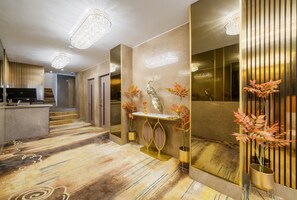 A modern hotel lobby with a reception desk, a decorative console table with vases, and a large mirror reflecting the interior. - Modern Mayfair Gem Two Bedroom Apartment H6 (London)