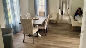 A dining area with a wooden table and chairs, a small side table with a bottle, and a view through a window with blue curtains. - 3BR, 4-Bed Home in Port Clinton (Port Clinton)