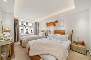 A modern hotel room with two beds, a vanity, and a view of the city.