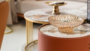 Un moderno salón con una mesa de centro de mármol, un reposapiés de cuero y una mesita auxiliar con marco dorado.