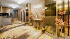 Un moderno vestíbulo de hotel con una mesa de recepción, una consola decorativa con jarrones y un espejo grande que refleja el interior.