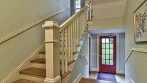 Una escalera de madera con barandillas blancas que conduce a una puerta roja con un ventanal.
