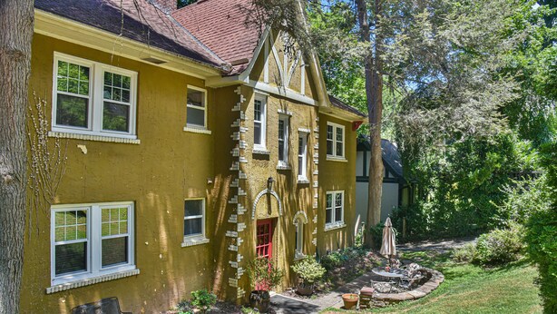 Una casa amarilla con varias ventanas, una puerta roja y un jardín con un banco y plantas en macetas.