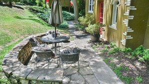 Un patio al aire libre con suelo de piedra, una mesa redonda, sillas de metal y una sombrilla.
