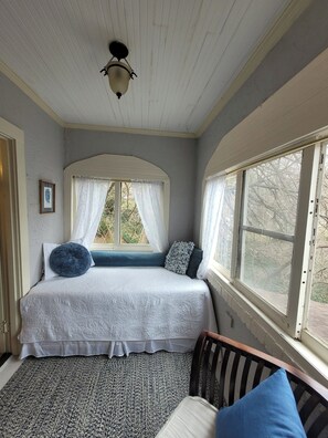 Une chambre avec un grand lit, une fenêtre avec des rideaux, une chaise en bois et un tapis à motifs.