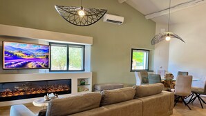 Een moderne woonkamer met een grote beige bank, een open haard, een flatscreen televisie en een eethoek met stoelen en een glazen tafel.