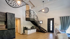 Een moderne woonkamer met een houten vloer, een zwarte trap, een grijze bank en een witte kast.