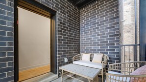 A small outdoor seating area with a table and two wicker chairs, a brick wall, and a wooden door.