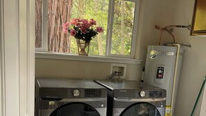 A laundry room with two front-loading washers, a water heater, and a window with a view of trees.