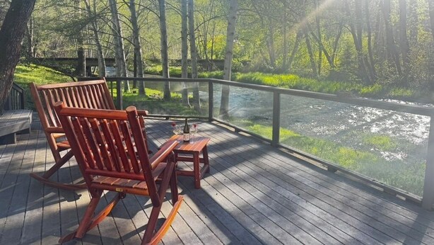A wooden deck with a bench and table overlooking a river, surrounded by trees.