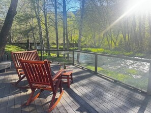 A wooden deck with a bench and table overlooking a river, surrounded by trees.