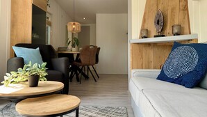 Una sala moderna con un sofá, dos sillones, una mesa de centro y una zona de comedor con mesa y sillas.