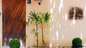 A villa entrance with a wooden door, potted plants, and a sign reading "Vila do Barão". - The House Plaza Hotel (Guarujá)