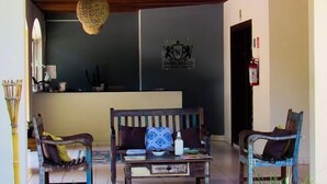 A reception area with a wooden bench, two chairs, a hanging light fixture, and a wall-mounted sign. - The House Plaza Hotel (Guarujá)