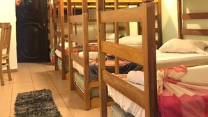 A dormitory room with bunk beds, a ceiling fan, a black door, and a small rug. - The House Plaza Hotel (Guarujá)