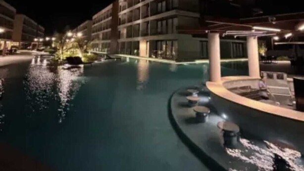 Ein Nachtblick auf einen Hotelpool mit einem kreisförmigen Wasserspiel und einer überdachten Sitzgelegenheit.