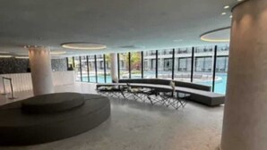 Ein großzügiger Innenbereich mit einer runden Sitzgruppe, großen Fenstern und einem Pool im Blick.