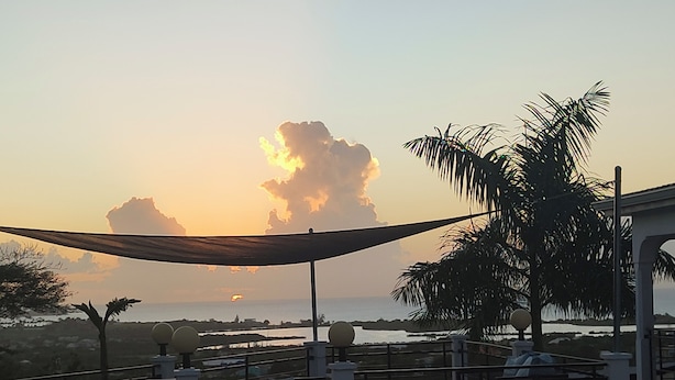 A terrace with a view of the sunset over the sea, palm trees, and outdoor seating. - Belvedere Holiday Home (St. John's)