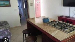 A kitchen with a marble countertop, a gas stove, a red cabinet, and a television mounted on the wall. - Belvedere Holiday Home (St. John's)
