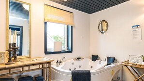 A bathroom with a large bathtub, a wooden vanity, a mirror, and a window with a view of greenery outside. - 5 Person Holiday Home in Snedsted (Snedsted)
