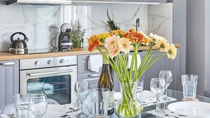 Eine moderne Küche mit grauen Schränken, einem Edelstahlbackofen und einem Essbereich mit einem Glastisch und Stühlen.