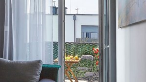 Ein modernes Schlafzimmer mit Bett, Sofa, Esstisch mit Stühlen und einer Schiebeglastür zu einem Außenbereich mit Garten und gedecktem Tisch.