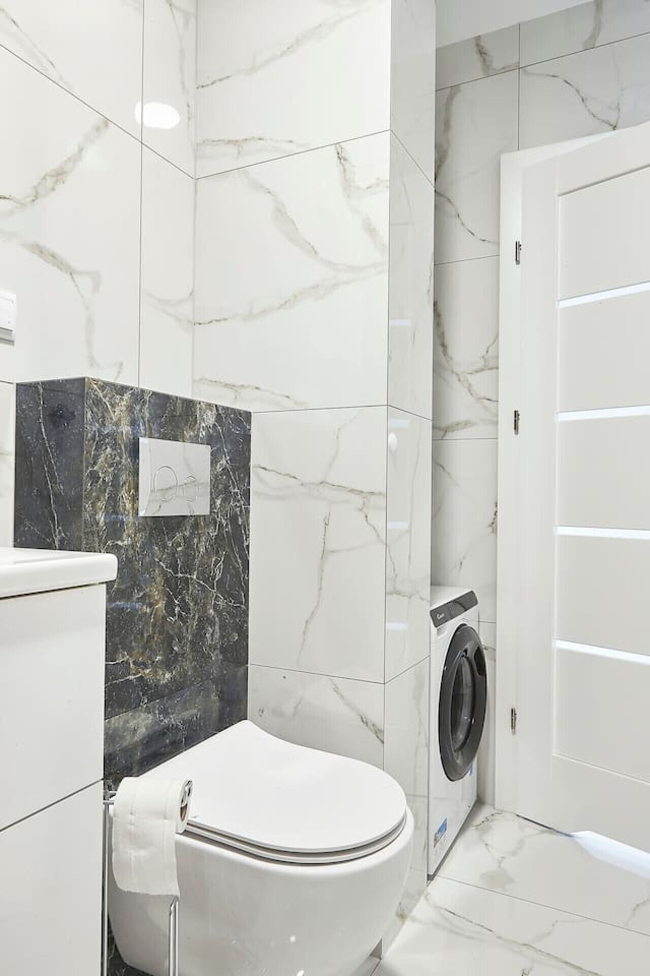 A modern bathroom with a toilet, a washing machine, and a marble wall.