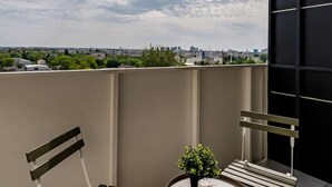 A balcony with a view of the cityscape, a round table with two chairs, and a small potted plant.