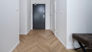 A hallway with a wooden herringbone floor, a dark door at the end, and a bench on the right.