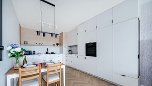 A modern kitchen with white cabinets, a wooden dining table, and a built-in oven.