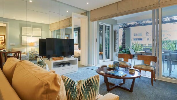 Una sala de estar moderna con un televisor de pantalla plana, asientos cómodos y un gran ventanal que da a un espacio exterior.