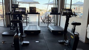 Un gimnasio con equipo de ejercicio, amplias ventanas y vistas a un puerto deportivo.